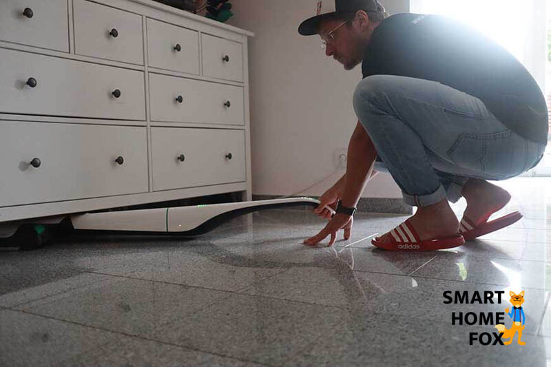 Man sieht, wie mit einem Akku-Saugwischer unterm Sofa geputzt wird.