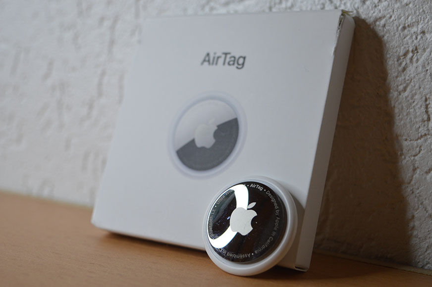 Airtag samt Verpackung sind vor einer weißen Wand zu sehen