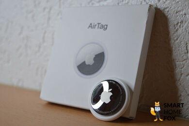 Airtag samt Verpackung sind vor einer weißen Wand zu sehen