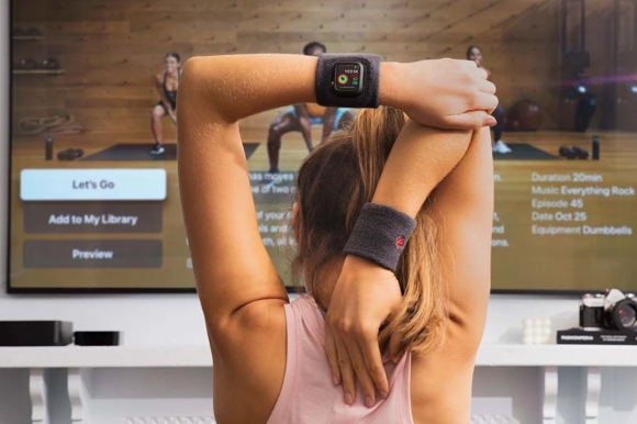 Frau steht vor Apple TV mit Fitness + Trainingsvideo und Apple Watch und dehnt sich