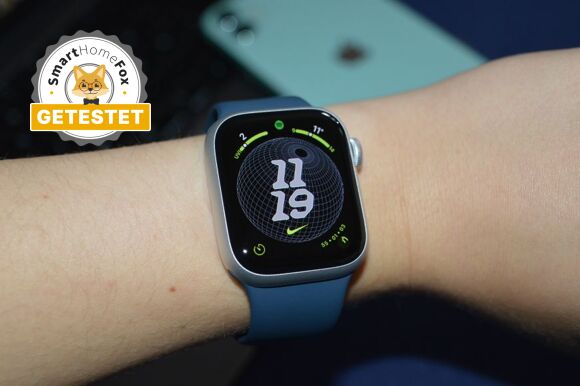 Apple Watch 9 mit Nike Globe Watchface und iPhone und Macbook im Hintergrund