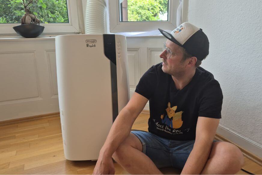 De'Longhi Pinguino PAC EX105 von der Seite mit sichtbaren Rollen und Abluftschlauch