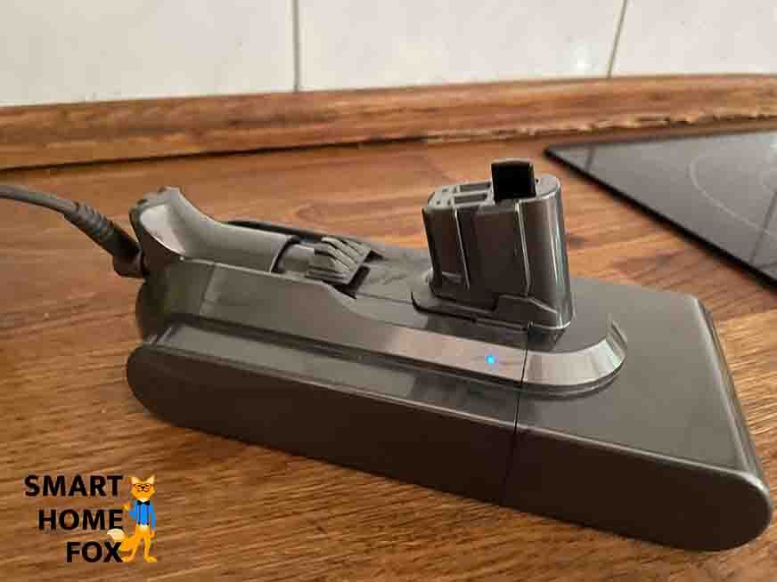 Der Dyson V15 Akku liegt auf einem Holztisch und wird per Kabel geladen.