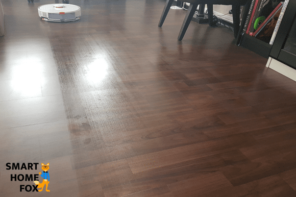 Man sieht, wie ein Saugroboter einen Parkettboden reinigt.