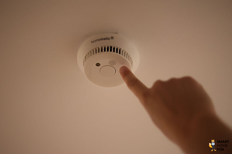 Finger zeigt auf an der Decke befestigten Homematic IP Rauchmelder