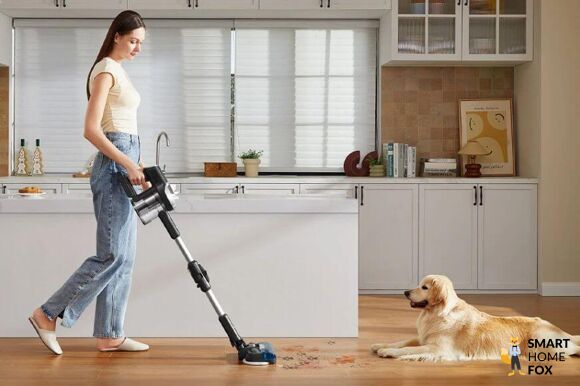 Der JIMMY JV9 Pro Aqua Wischsauger steht in einer Station an der Wand im Wohnzimmer, der Boden ist sehr sauber und das Wohnzimmer ist dank dem Wischsauger sehr gepflegt.