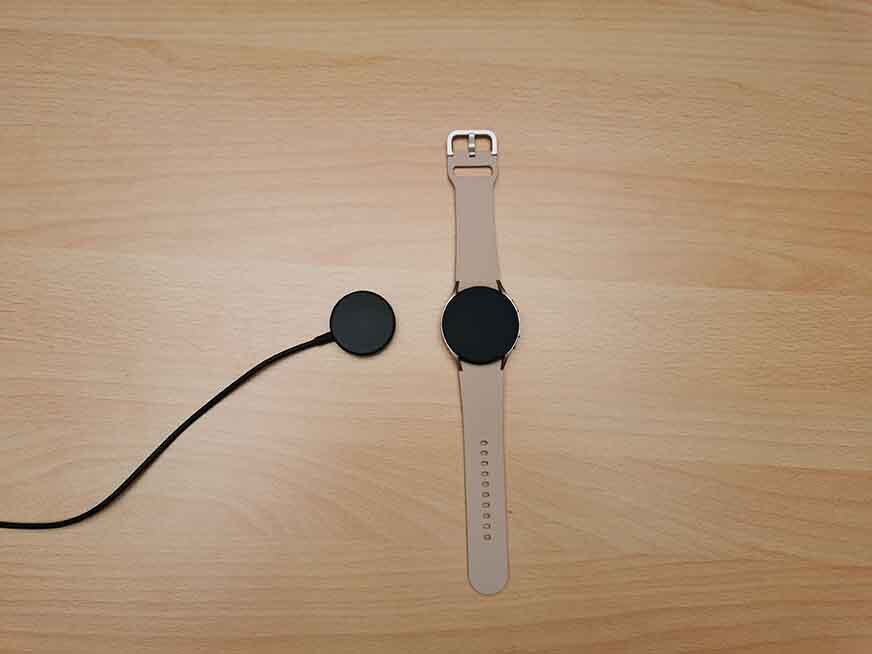 Man sieht die Samsung Galaxy Watch 4 neben ihrem Ladepad. 