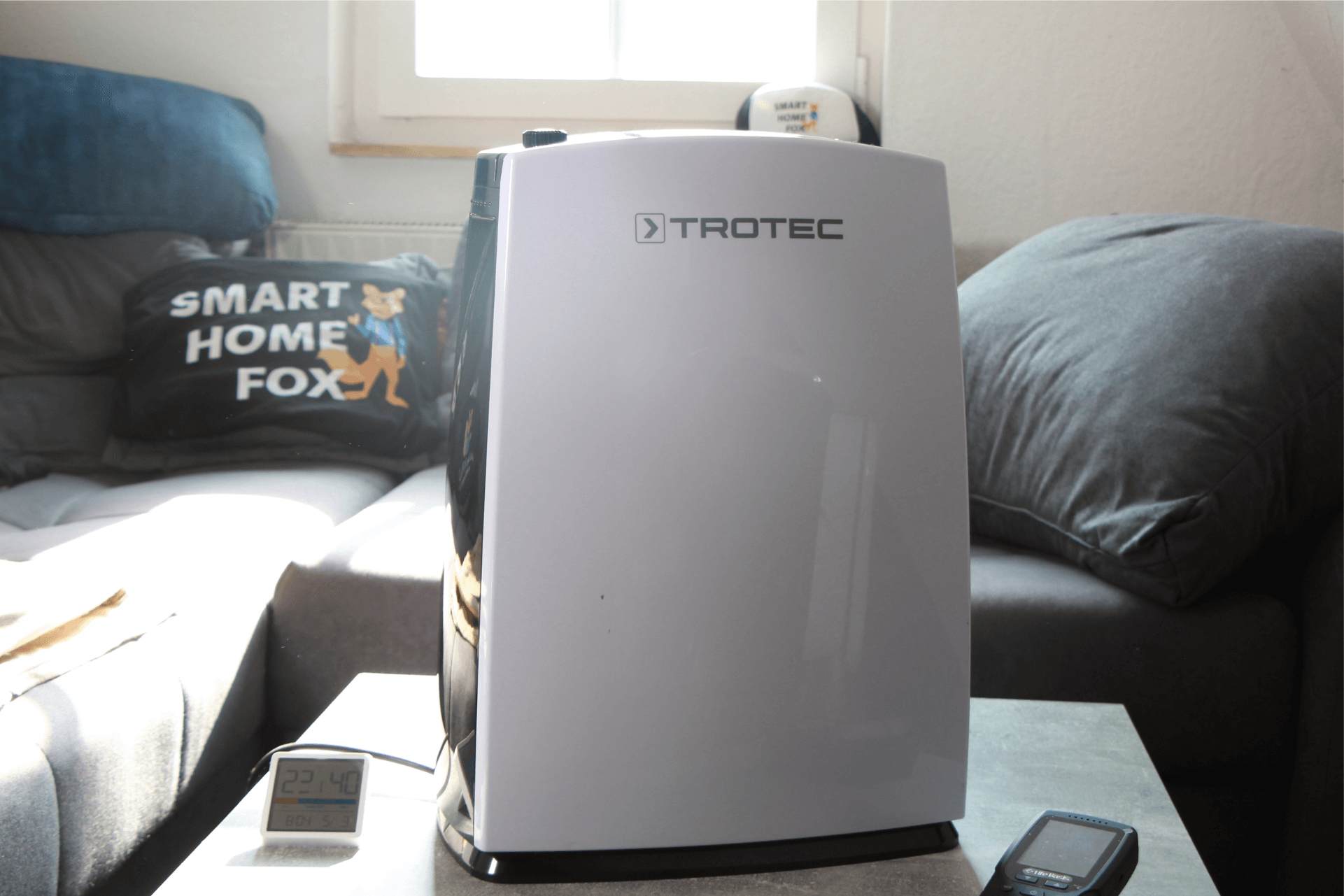 Der Trotec TTK 52 E Luftentfeuchter steht auf einem Couchtisch vor einer Couch.