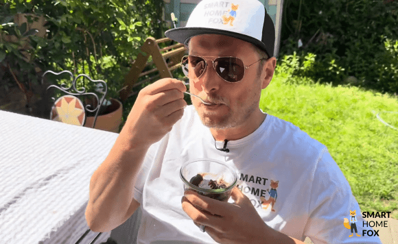 Smart Home Fox Experte genießt selbstgemachtes Eis aus der Ninja Creami Deluxe im Garten bei Sonnenschein.