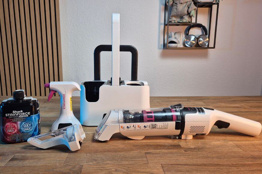Der Shark Stainforce Fleckenreinigungsgerät ist bei Smart Home Fox im Test, samt Zubehör, Aufsätzen, Reinigungslösung auf einem Tisch zu sehen.