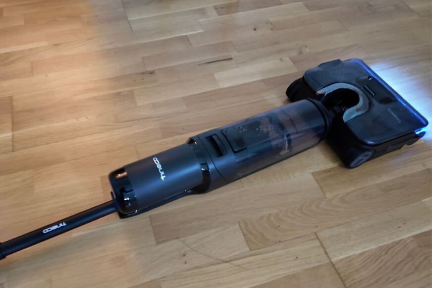 Der Tineco Floor One S7 Stretch Steam Plus mit Dampf- und Selbstreinigungsstation in Schwarz-Silber liegt flach auf dem Boden.