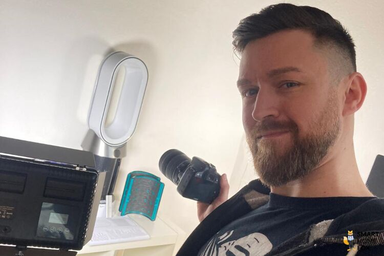 Autor Profilbild Alex steht vor einem Luftreiniger und fotografiert ihn.