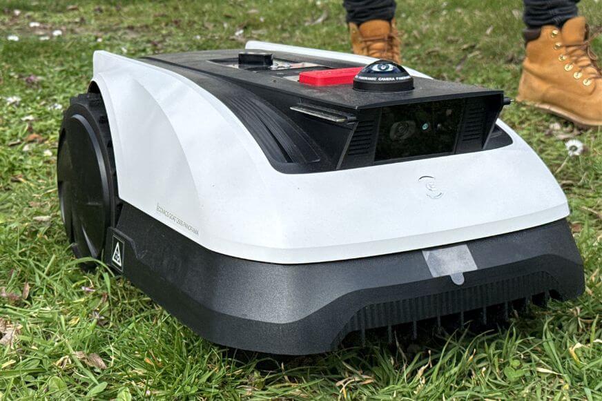 Der Ecovacs GOAT O500 Panorama Mähroboter steht im Test im Garten, und mäht den Rasen, während der Experte ihm beim testen zusieht.