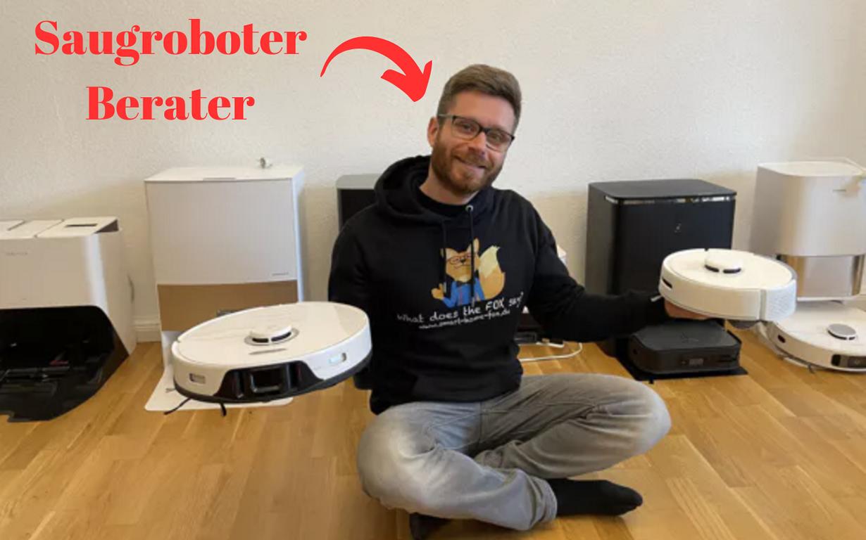 Der Saugroboter Berater ist zwischen zahlreichen Saugrobotermodellen sitzend zu sehen und er hält 2 Saugroboter hoch.